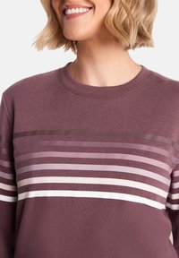 Smiling person with short blonde hair wearing a mauve sweater featuring horizontal stripes in varying shades of pink and white.