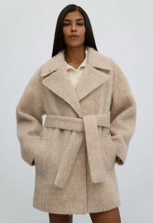 Beżowy wełniany płaszcz z paskiem w talii, szerokimi klapami i bocznymi kieszeniami. Miękka faktura i długość do połowy uda.