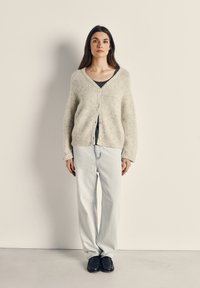 Helehall pehmev kardigan V-kaelusega ja nööbiga, koos tumeda ülikonna ja helesiniste sirgete pükstega, lõpetades mustade kingadega.