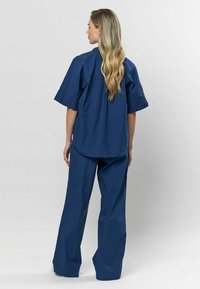 Tumesinine meditsiiniline ülikond, mis on valmistatud kergeks kangast. Omab lühikesi varrukaid, laia lõike ja siledat õmblust mugavuse tagamiseks.