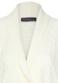 Witte gebreide cardigan met een sjawl kraag, met kabelbreipatronen. Het label zegt "FELIX HARDY" in donkerblauw en groen.