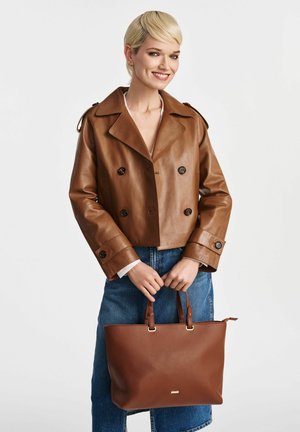 Brązowa skórzana kurtka typu cropped z podwójnymi zapięciami, zestawiona z niebieskimi dżinsami i usztywnioną brązową torbą tote ze złotymi akcentami.