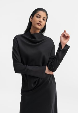 Maglia nera con collo a cowl, maniche lunghe, texture liscia e vestibilità ampia. Presenta una drappeggio sottile e un dettaglio a polsino stratificato.