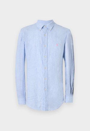 Camisa de manga larga azul claro con rayas verticales blancas, cuello abotonado y pequeño logo bordado en rosa en el pecho izquierdo.