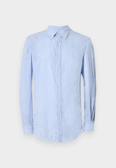 Ανοιχτό μπλε πουκάμισο με μακριά μανίκια και κάθετες λευκές ρίγες, γιακάς με κουμπιά και μικρό ροζ κεντητό λογότυπο στο αριστερό στήθος.