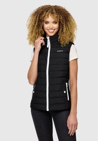 Gilet matelassé noir avec un col montant, fermeture éclair blanche, deux poches avant et un logo sur le côté gauche. Porté par-dessus une chemise de couleur claire.