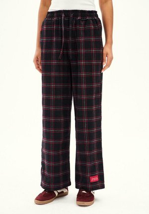 Luźne spodnie w czarno-czerwoną kratę, z wiązanym pasem, noszone z białą bluzką i bordowymi trampkami z gumowymi podeszwami.