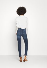 Úzké tmavě modré džíny s vysokým pasem, vybavené zadními kapsami a roztrhanými lemy, doplněné bílou košilí s dlouhým rukávem.