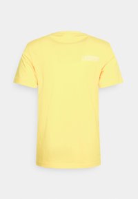 Žluté bavlněné tričko s krátkými rukávy, s malou bílou grafikou umístěnou na horní části zad. Hladká textura, standardní kulatý výstřih.
