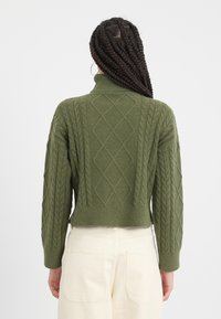 Pulover tricotat de culoare verde închis cu guler înalt, având un design texturat de tip cable-knit și tiv cu nervuri, croi scurt și mâneci lungi.