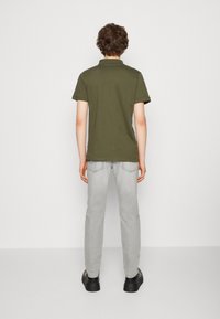 Olivově zelená polo košile s krátkým rukávem, spárovaná se světle šedými džíny a černou obuví. Jednoduchý design, žádné viditelné loga ani vzory.