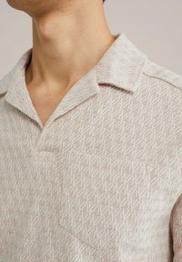 Beige, rövid ujjú, galléros ing, textúrált gyémántmintával, egyszálú zsebből áll, és puha, könnyű anyagból készült.