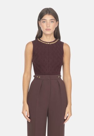 Top sin mangas burdeos con patrón texturizado, combinado con pantalones de tiro alto y plisados con detalles de botones dorados.