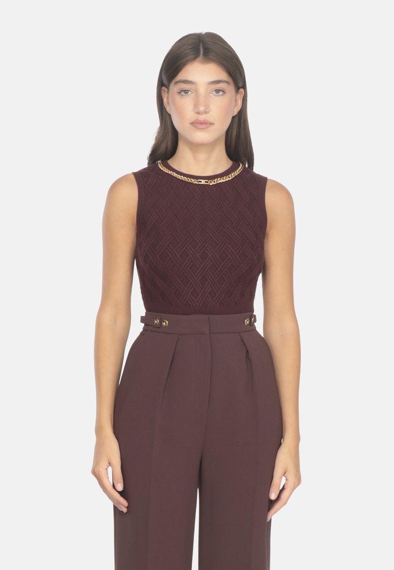 Top sin mangas burdeos con patrón texturizado, combinado con pantalones de tiro alto y plisados con detalles de botones dorados.