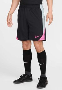 Pantaloni sportivi neri con accenti rosa e azzurri, dotati di una cintura elastica e strisce laterali, abbinati a calze nere fino al ginocchio e scarpe.