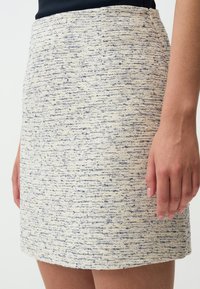 Gewebter Creme-Rock mit blauen Sprenkeln, gerader Schnitt, strukturierter Stoff, mittlere Oberschenkellänge, mit einem verdeckten Reißverschluss an der Seite.