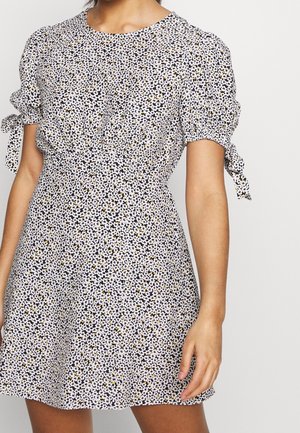 Vestido de manga corta con escote redondo, que presenta un estampado floral en negro, blanco y amarillo. Los lazos en las mangas añaden un detalle adicional.