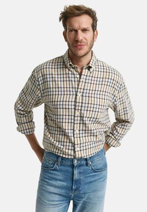 Camisa de cuadros en tonos beige, azul y marrón. Tejido de algodón, mangas largas, bolsillo en el pecho, combinada con jeans de color azul claro.