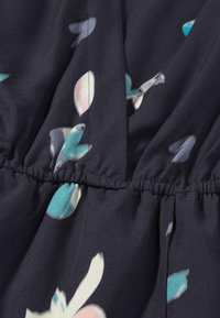 Stoff mit floralem Muster in dunkelblauem Marineblau und elastischer Raffung. Zeigt abstrakte, hellfarbige Blätter in Blau- und Rosatönen. Weiche Textur.