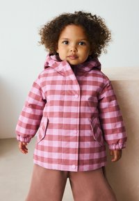 Roze en lichtroze geruite regenjas met capuchon, elastische manchetten en knopen, gecombineerd met bruine broek. Glad, waterafstotend materiaal.