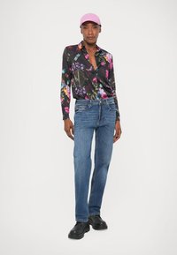 Blusa nera floreale, jeans blu e scarpe nere. La blusa presenta motivi floreali colorati, maniche lunghe e colletto.