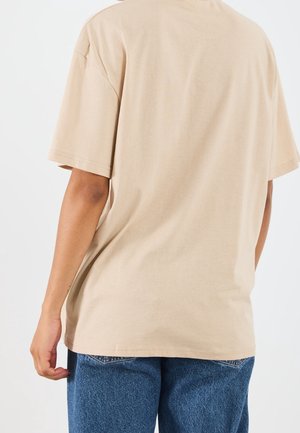 T-shirt beige in cotone con maniche corte e vestibilità comoda, caratterizzata da una texture liscia e una scollatura rotonda, mostrata da dietro.