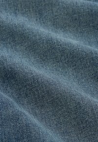 Close-up van gestructureerde blauwe denimstof met zichtbaar keperbinding patroon en zachte plooien.