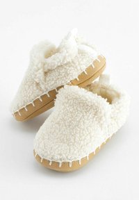 Białe, puszyste klapki z miękkiego materiału shearling z brązową zamszową podeszwą i białymi detalami w szwach. Posiadają dekoracyjną kokardę na górze.