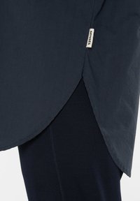 Dark blue fabric shirt with a curved hem, featuring a visible label reading "SENSES" on the side. Smooth texture and lightweight design.