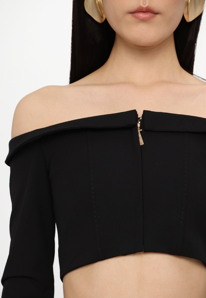 Crop top noir sans manches avec fermeture éclair, présentant une coupe ajustée et des détails de couture doublée. Texture lisse.