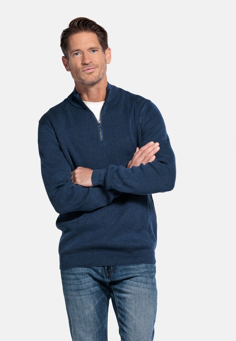 Donkerblauw gebreid kwart-rits pullover met een gestructureerd patroon, lange mouwen en een witte onderhemd, gecombineerd met spijkerbroek.