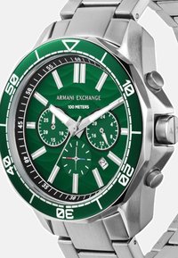 Ura iz nerjavnega jekla z zelenim vzorčastim številčnico, srebrnimi poudarki, belimi kazalci in podštevci. Vodoodporna do 100 metrov.