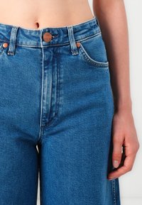 High-waisted blue denim jeans with a faded finish. Features copper-button closure, two front pockets, and a relaxed fit through the legs.