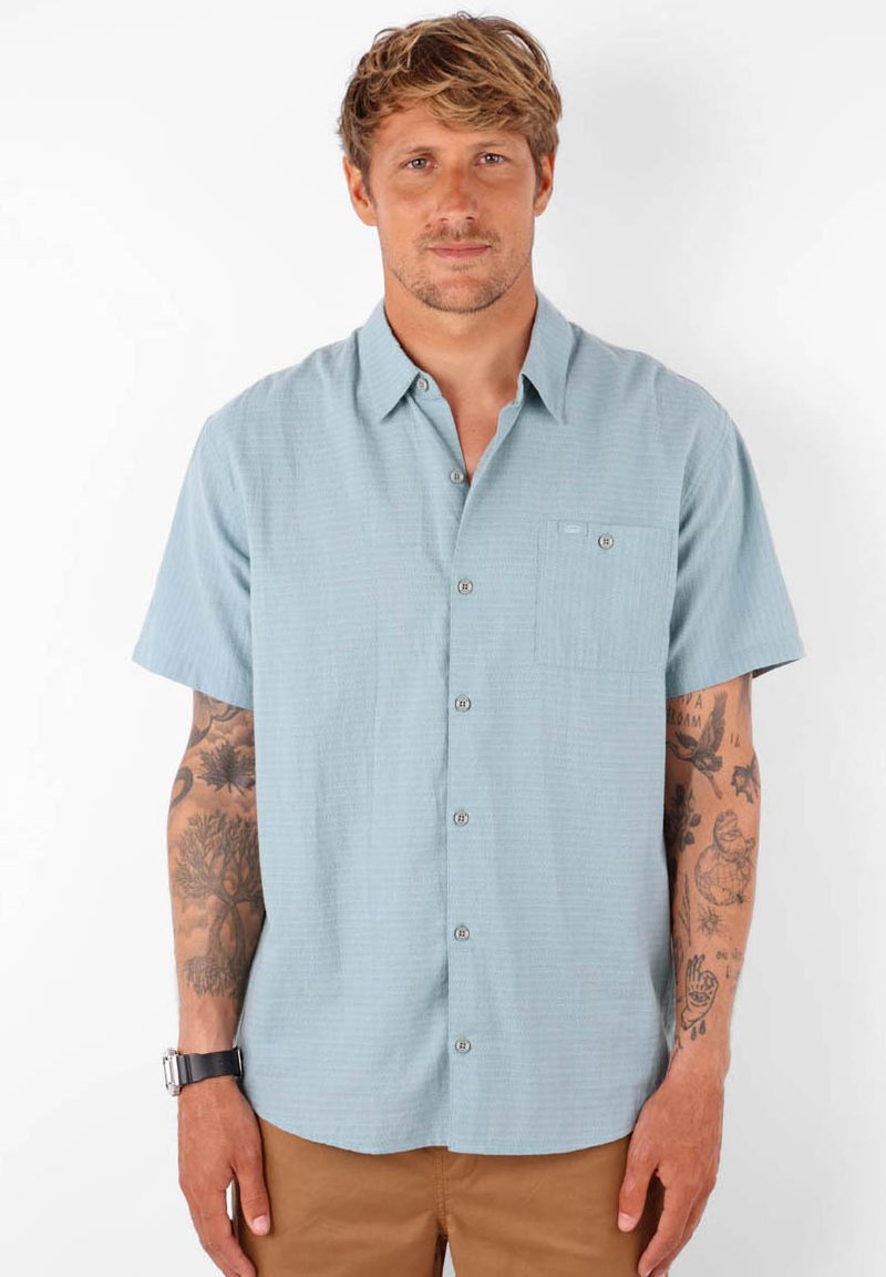 Chemise à manches courtes bleu clair, avec des boutons, dotée d'une poche plaquée et d'un tissu texturé. Elle présente un col standard et un motif horizontal subtil.