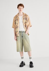 Tan kortemouw shirt met blauwe en groene bloemenpatronen, witte tanktop, vervaagde groene denim shorts, zwarte platform schoenen en gestreepte sokken.