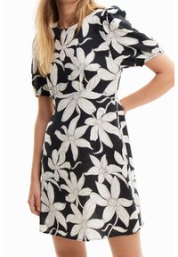 Blumenkleid mit schwarzem Hintergrund, das weiße Blumenmuster zeigt, kurze Puffärmel und einen runden Ausschnitt hat, aus leichtem Stoff gefertigt.