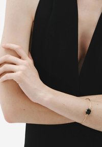 Pulsera de oro con una piedra negra central, que presenta un diseño elegante y minimalista. La pulsera tiene un acabado suave y una forma delicada.