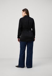 Black long-sleeve shirt with collar and belted waist, made of a smooth fabric. Paired with wide-leg blue denim pants.