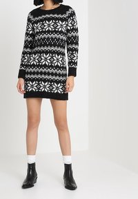 Abito in maglia bianco e nero con motivo a fiocchi di neve, maniche lunghe, scollatura tonda e una finitura leggermente texturizzata.
