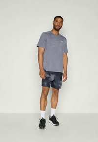 Camiseta atlética gris con un patrón sutil, combinada con pantalones cortos azul marino oscuros con un degradado. Zapatillas negras y calcetines cortos blancos completan el look.