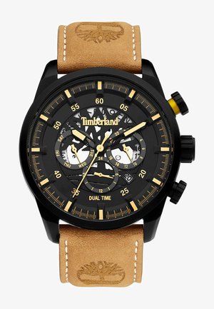 Montre chronographe noire avec un cadran transparent, des accents dorés et un affichage double heure. Elle possède un bracelet en cuir marron clair avec des détails cousus.