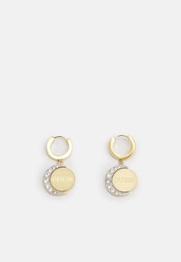 Des boucles d'oreilles en métal doré en forme de cr�éole présentent des disques ronds avec une gravure "GUESS" et un design en croissant orné de strass transparents.