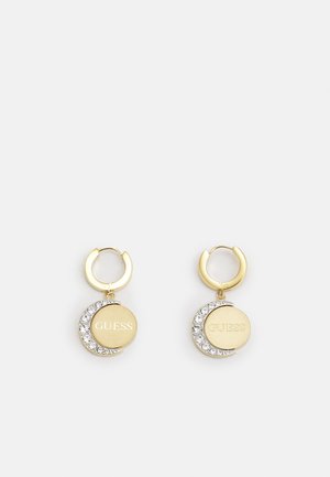 Zelta krāsas riņķveida auskari, kuros ir apaļi diski ar "GUESS" gravējumu un pusmēness formas dizains, ko rotā caurspīdīgi rhinestones.