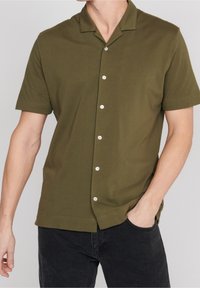 Olivgrön kortärmad skjorta med krage och knäppning fram, med vita knappar, tillverkad av ett mjukt, texturerat tyg. Avslappnad passform.