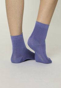 Calcetines morados con ribete y acabado texturizado, con puño enrollado y una sutil marca lateral. Diseño a la altura del tobillo.