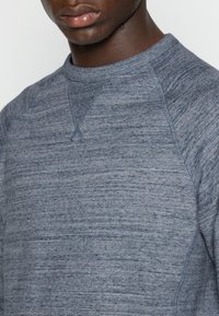 Grijze crewneck sweatshirt met een gestructureerd, gemêleerd patroon. Beschikt over raglanmouwen en ribgebreide boorden rond de halslijn en onderrand.