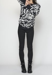 Černý a bílý vzorovaný pletený svetr s huňatou texturou, spárovaný s černými skinny džíny a černými šněrovacími kotníkovými botami.