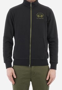 Černá fleecová bunda na zip s vysokým límcem, dvěma předními kapsami, zelenými detaily na zipu a vyšívaným logem na hrudi. Materiál ze směsi bavlny.