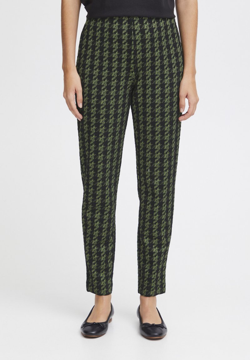 Pantalon pied-de-poule noir et vert avec une coupe slim, doté d'un tissu texturé et d'une ceinture lisse, associé à des ballerines noires.