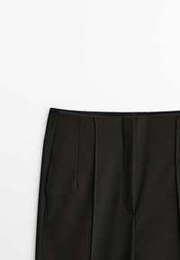 Black tailored trousers made of smooth fabric; features front pleats and a structured waistband. Minimalist design, no patterns or hardware.